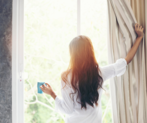 Woman waking up early looking out the window drinking coffee for a productive morning routine