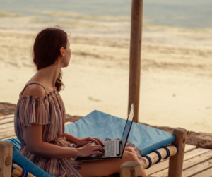 A woman sitting at the beach remote working on her laptop