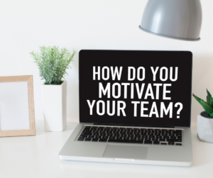 A laptop on a table with a screensaver reading "how do you motivate your team?"