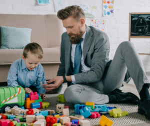 A man is a suit playing with his son and his toys 
