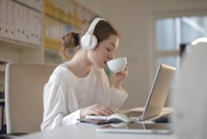 Woman in white shirt on laptop drinking coffee while listening to music on her laptop