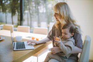 Blonde woman with baby on her lap working on her laptop