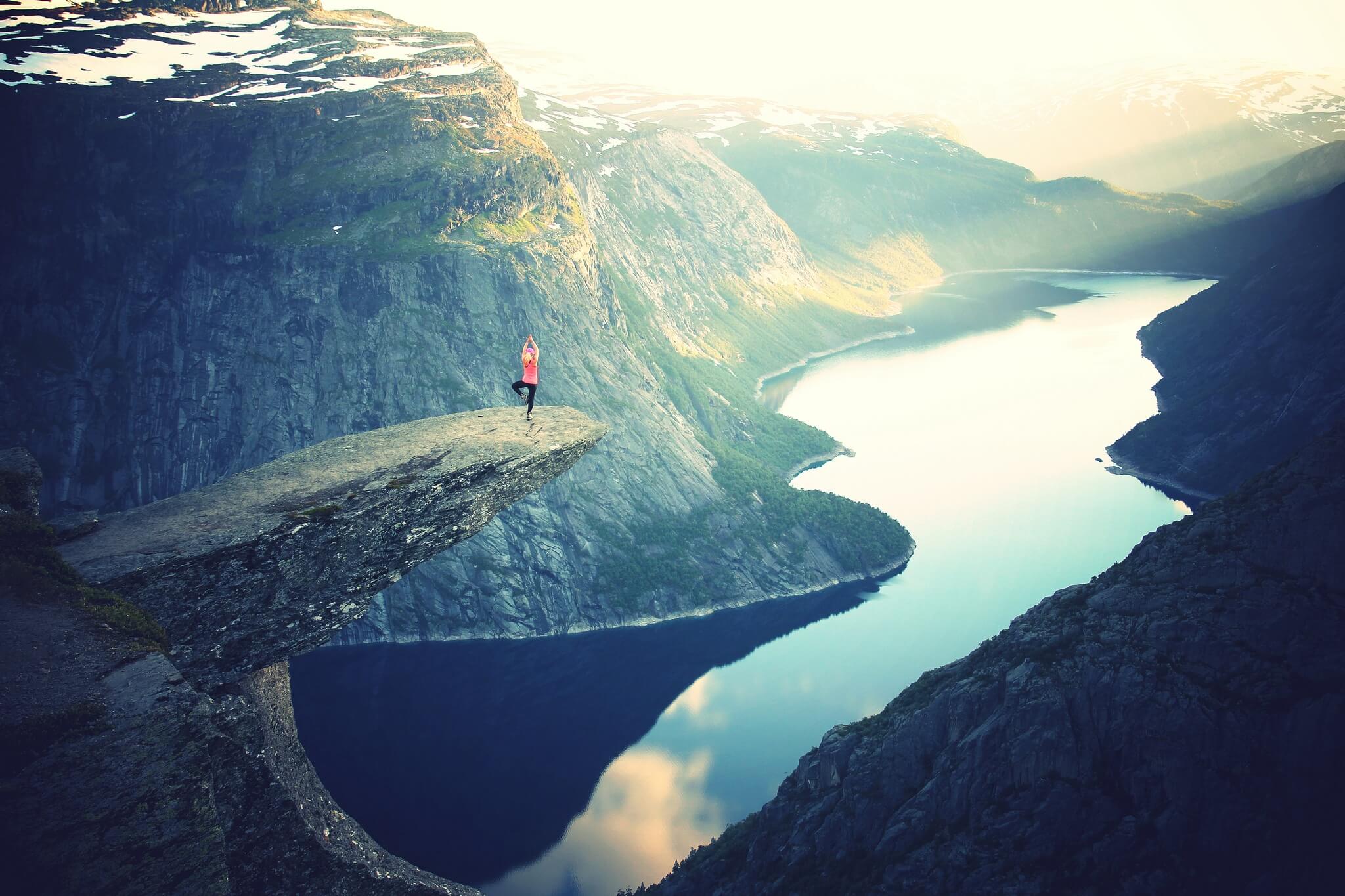 Someone standing in a yoga pose on a very scenic mountain ledge over looking a large lake