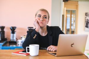 A blonde woman sitting at her desk with coffee and a laptop looking bored