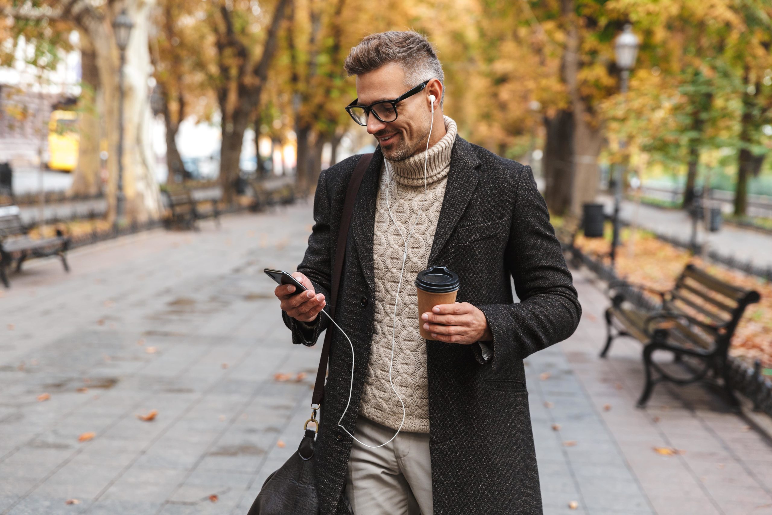 AVirtual blog practical guide working with virtual assistant smiling man with grey hair walking down the street looking at his phone wearing earphones